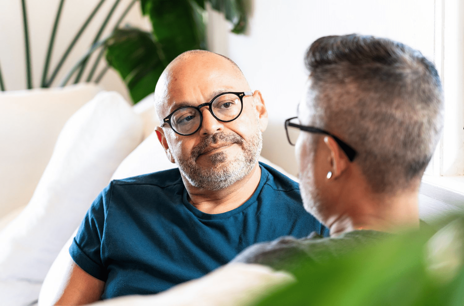 A man listens attentively to his partner on their couch at home.
