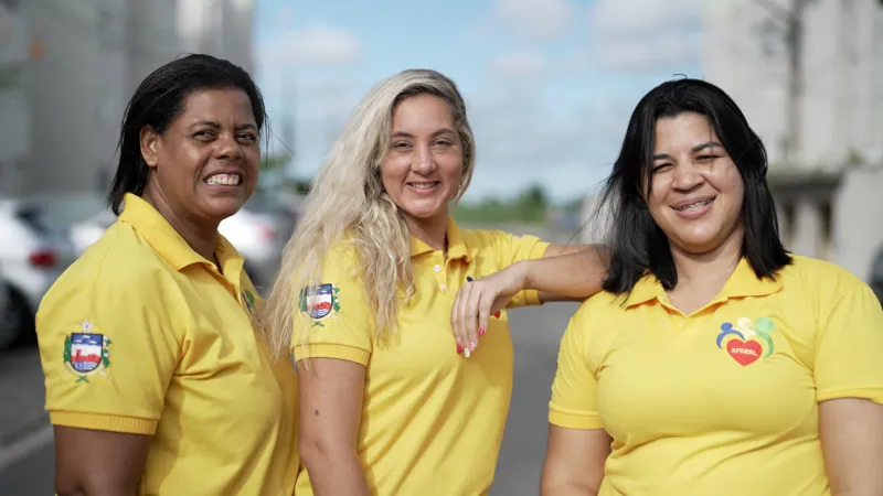 Felix Lima/INLIBER News Brasil Lenice França, Anne Caroline Rosa and Rute Freires stand together and smile. They are looking towards the camera. All are wearing yellow polo shirts.