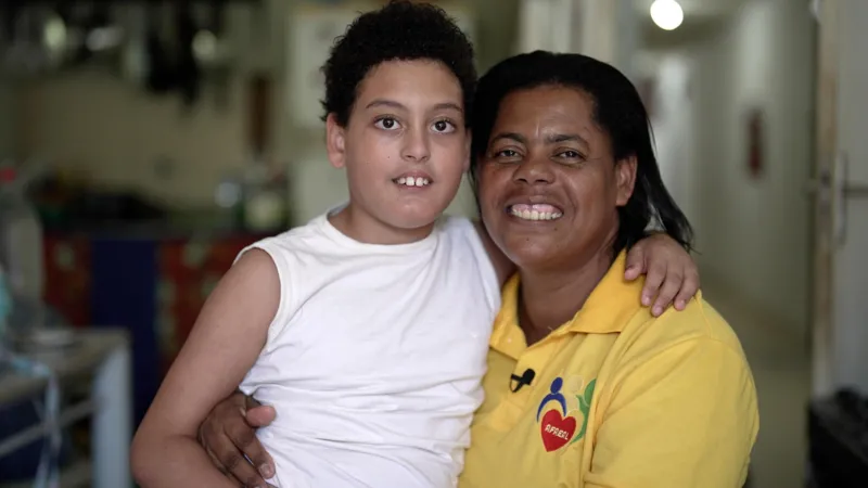 Felix Lima/INLIBER News Brasil Enzo and Lenice França smile at the camera. Lenice is wearing a yellow polo shirt and Enzo is wearing a white vest.