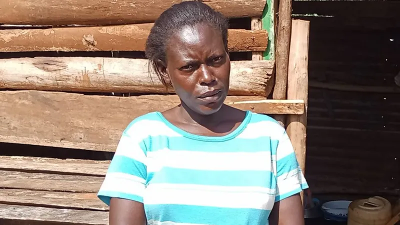 Carolyne Odour in a blue and white horizontal striped T-shirt standing outside a wooden plank house.