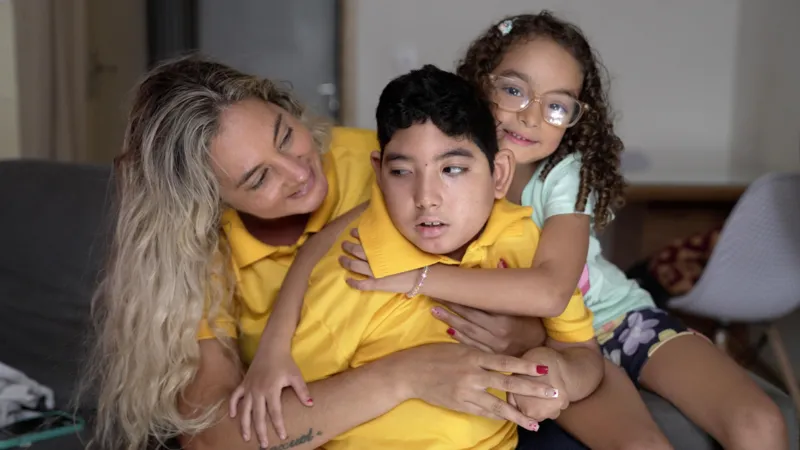Felix Lima/INLIBER News Brasil Anne Caroline Rosa with her children Moisés and Maria. Anne Caroline and Moisés are wearing matching yellow polo shirts. Maria is wearing a white shirt.