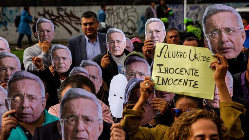 Antonio Cascio/SOPA Images/LightRocket via Getty Images Uribe supporters gather in front of the courthouse during the rally. They are wearing masks of Uribe's face and holding a sign declaring his innocence. 