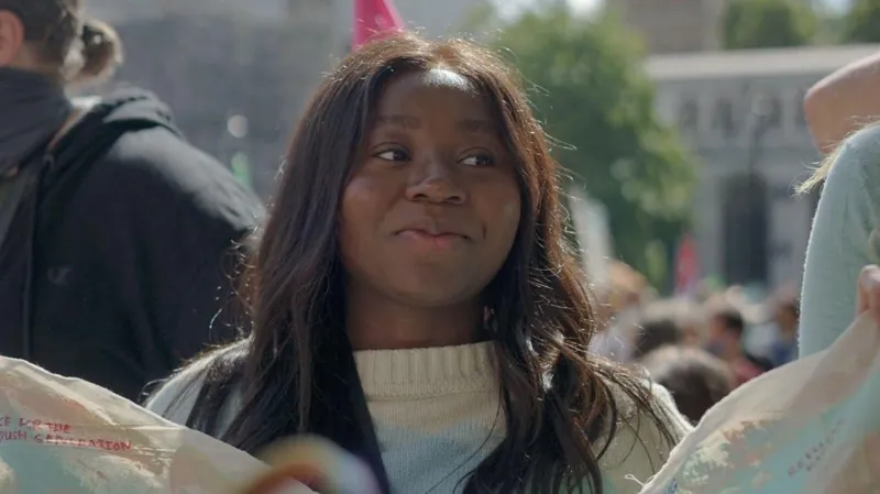 Daze Aghaji Daze Aghaji, a young woman in a white jumper, with long hair, smiling at a demonstration