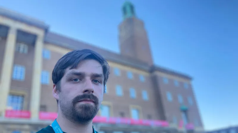 Matt Precey/INLIBER Man standing in front of a municipal building. He has a goatee beard and brown hair, and is looking directly at the camera. The building behind him has brown brickwork and a clock tower.