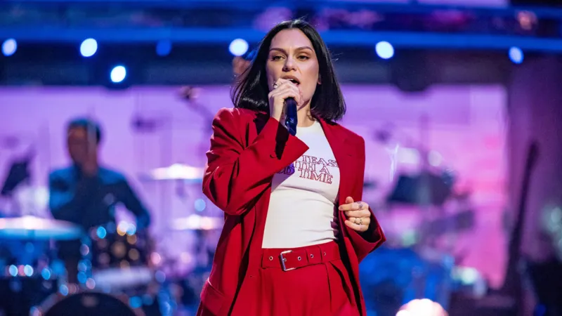 Jessie J, qizil kostyumda sahnada, orqasida band