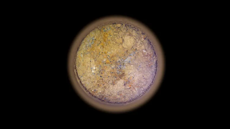 NASA/JPL Image of a core of rock taken from Mars. The image shows a circular slice through of the rock sample against a black background. The sample is orange and dotted with white, grey and black marks.