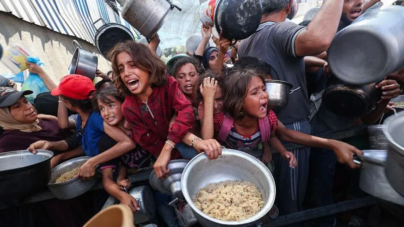 AFP via Getty Images A bustling crowd of crying children hold out pots to be filled with food. 