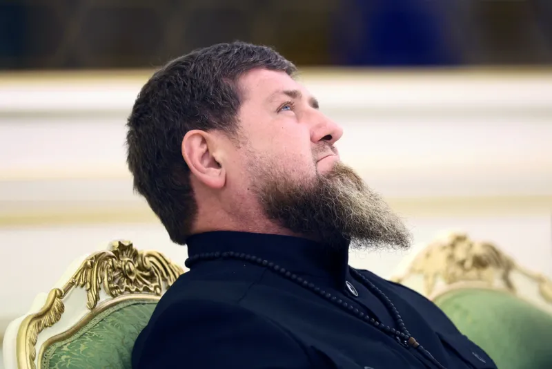 Reuters Ramzan Kadyrov on an ornate chair with a full, long beard looking slightly upward with a contemplative expression. He’s wearing a dark-colored shirt with a high collar. Around his neck is a string of black prayer beads or a bead necklace