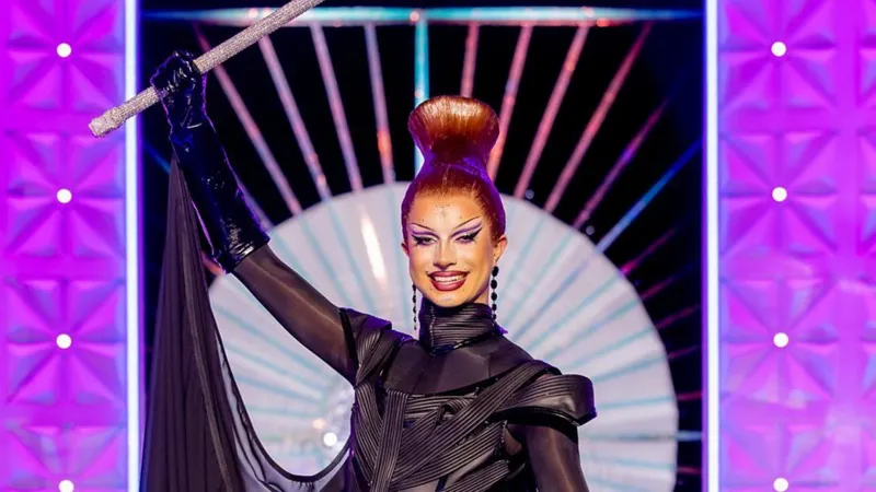 Bones berpose di panggung mengenakan gaun hitam dengan tongkat di tangan