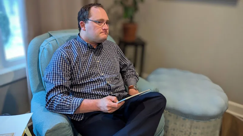 Nicholas Strahl Nicholas Strahl, wearing glasses and a checked shirt, sits in an armchair holding a tablet.