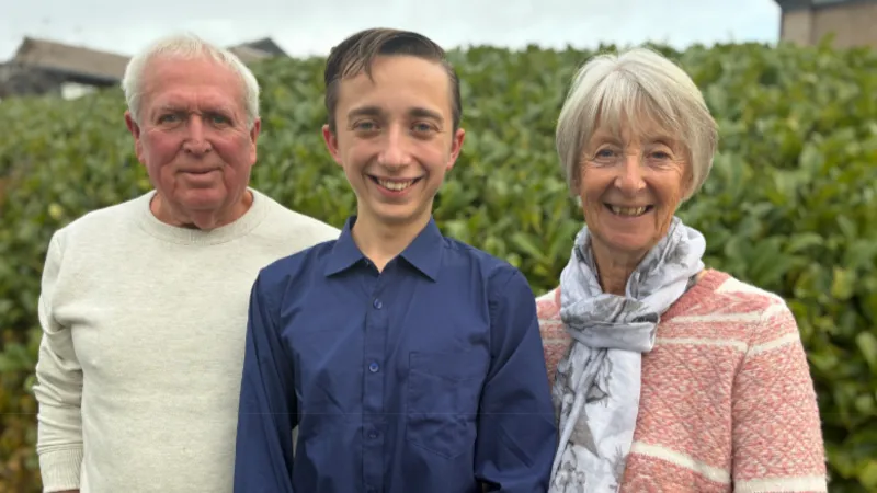 Adrian, Daniel and Jill in a midshot in front of a tall hedge all smiling to camera.