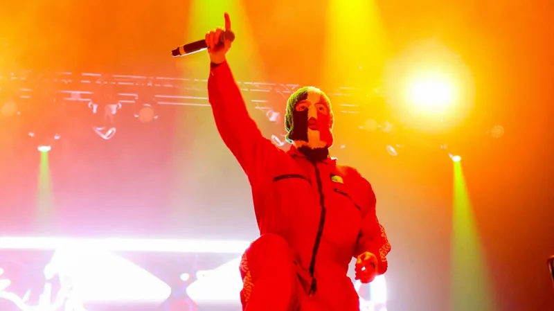 Getty Images DJ Próvaí of the band Kneecap poses with one arm raised in the air, while wearing a balaclava in the colours of the Irish flag, on stage at the Coachella festival in 2025