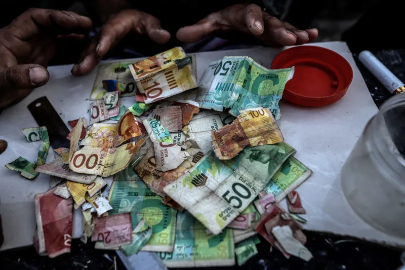 Anadolu via Getty Images Palestinians repair old and worn-out banknotes as the enclave runs out of hard currency on June 02, 2025, in Gaza City