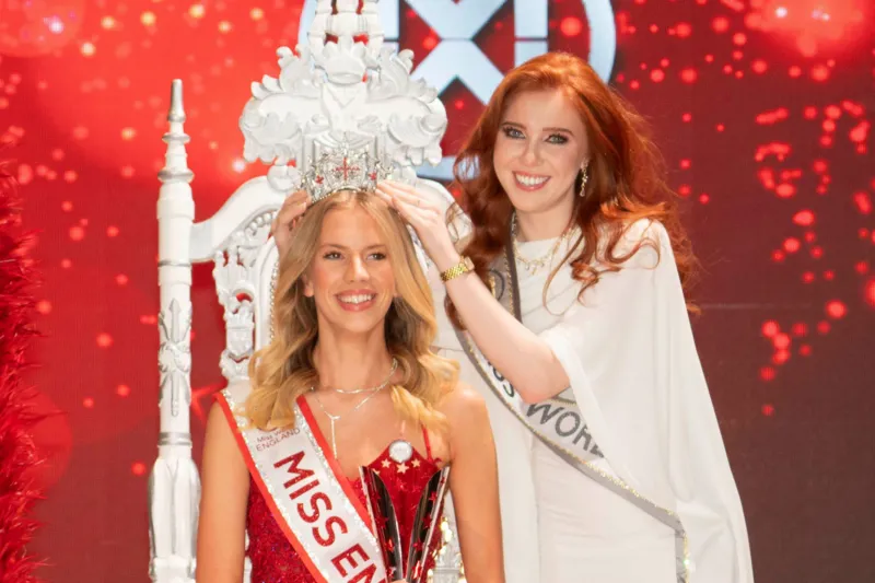 Alan Strutt/Miss England Grace Richardson wearing a red dress being presented with a tiara by a woman wearing white