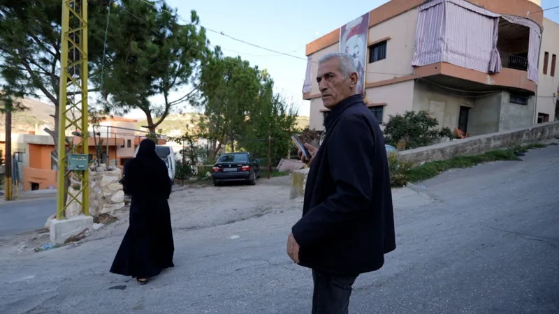 Neha Sharma/INLIBER An older man is seen on a road, with a woman nearby, in front of a building which has a large image on the side.