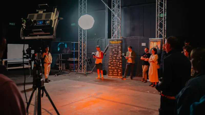 BFS Students are on an interior sound stage. There are lights, cameras, and a large screen.