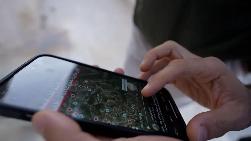 Neha Sharma/INLIBER Hands hold a mobile phone, on which can be seen a satellite image with red and blue dots marking locations.