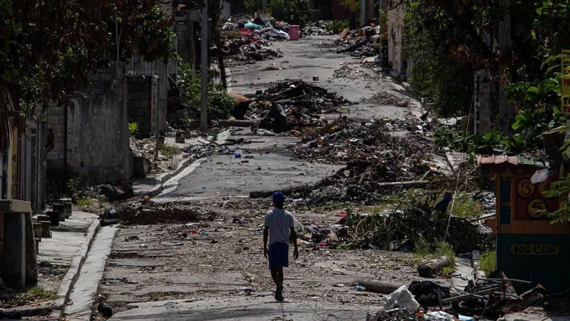 CLARENS SIFFROY/AFP via Getty Images A wide shot of a lone figure walking along a road covered in debris in the Delmas 30 neighborhood in September 2025