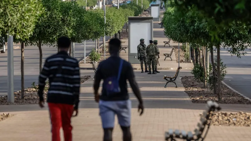 AFP via Getty Images Two men walk down an empty road towards a group of soldiers, who are standing guard