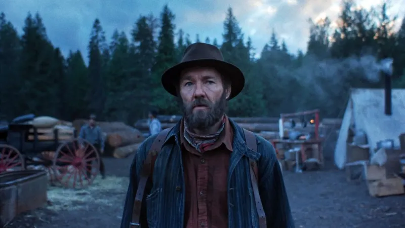 Netflix Joel Edgertonin Train Dreams, wearing a hat and looking ahead, with trees in the background