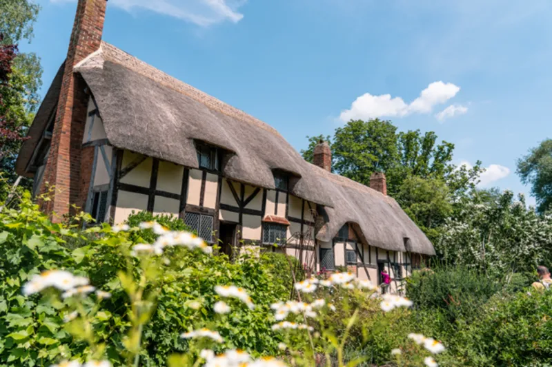 Shakespeare Birthplace Trust A thatched 15th-century house surrounded by flowers and trees. The walls are white with brown beams