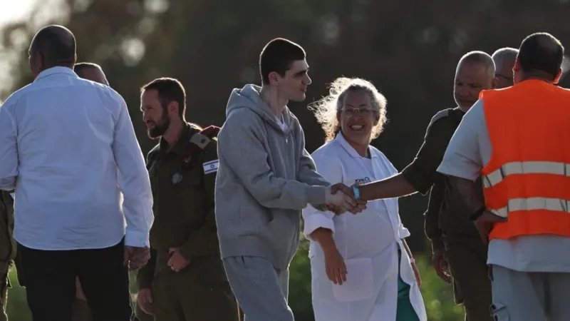 EPA Maxim Herkin, wearing a grey, jumpsuit shakes hands with an Israeli officer as a medic in a white overcoat looks at him smiling