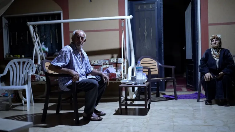 Neha Sharma/INLIBER An older man and woman sit on a tiled area outside a house, after dark.