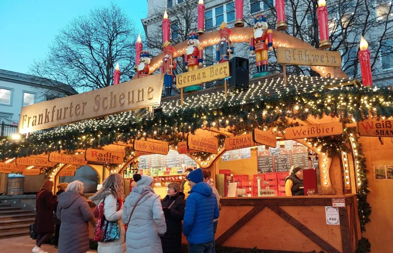 A Bavarian-style wooden stall at a Christmas market, decorated with fairy lights and signs for drinks