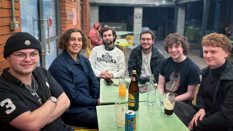 A group of six young men are sitting around two tables in a pub in Dublin
