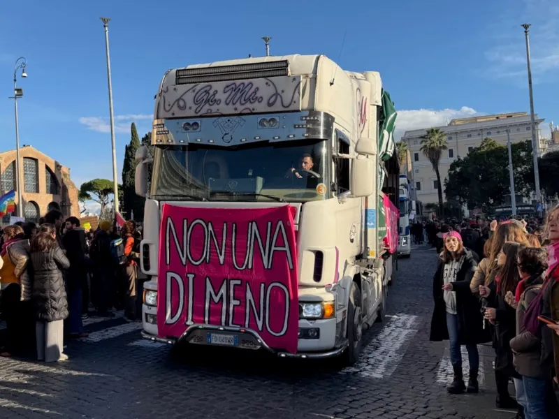 A lorry surrounded by crowds of largely women displaying a banner which says Non Una Di Meno (Not One Less).