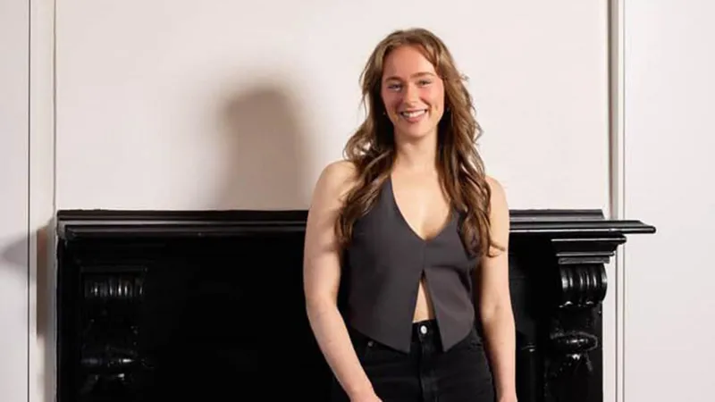 Maddi Mathers A woman wearing a grey waistcoat and black pants smiles at the camera. She is posing for a headshot type picture.
