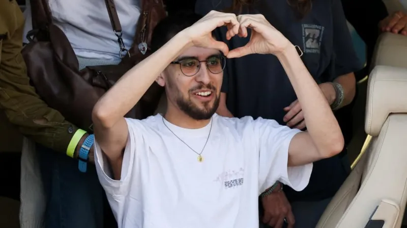 Reuters Evyatar David, wearing a white T-shirt, a necklace, glasses and sporting a beard, makes the sign of a heart with his hands just above his head 