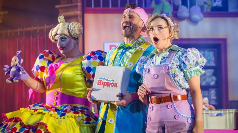Terry Gleed wearing a white wig and blue-and-white dame costume on stage with scenery in the background.