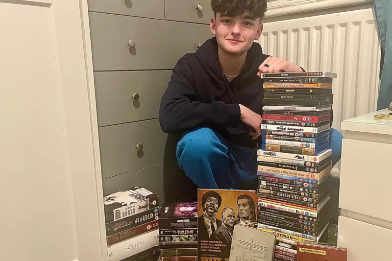 Declan holding DVDs with stacks of cases around him.