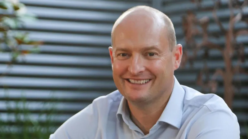 A smiling man in a light shirt, photographed indoors