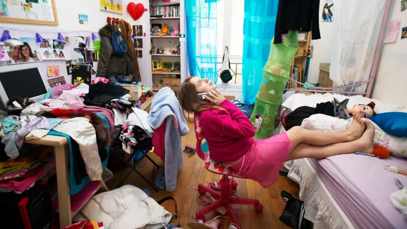 A woman on the phone in a cluttered bedroom