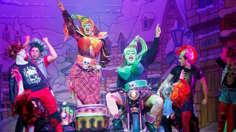 Grove Teatri sahnasida besh-olti aktyor rangli kostyumlarda, tepalardan biri motorli mototsiklga o‘ralgan