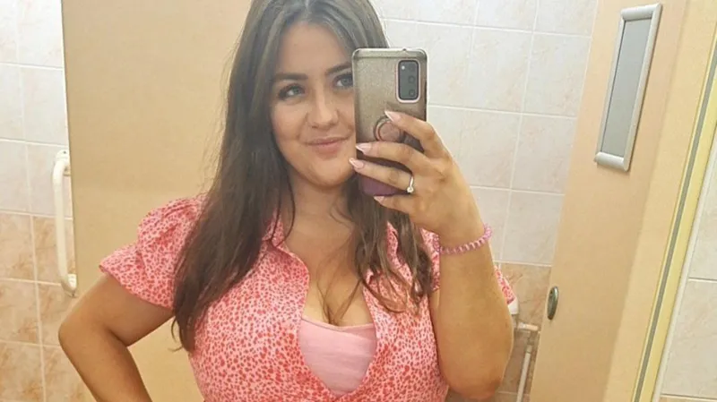 Melissa Ashcroft wearing a pink dress, smiling in a mirror