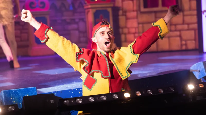 Ben Parsley in a yellow and red jester outfit backstage with arms outstretched.
