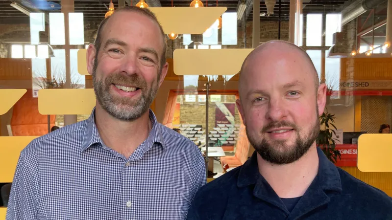 Майлз Арнотт слева и Гайлс Майл справа улыбаются; они в шортах, за ними окно с яркими рисунками.