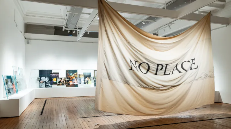 A white ceiling with a black NO PLACE sign and surrounding artworks