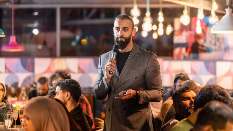 CN Photography Qizil yorug‘liklar ostida turadigan erkak jurnalist mikrofonga tushmoqda