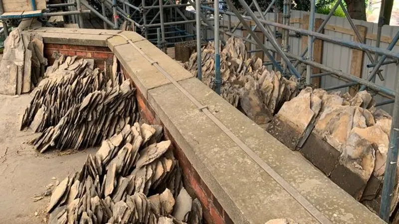 North Northamptonshire Council Piles of slate tiles on the edge of roof, showing scaffolding to the right and roof ledges. 