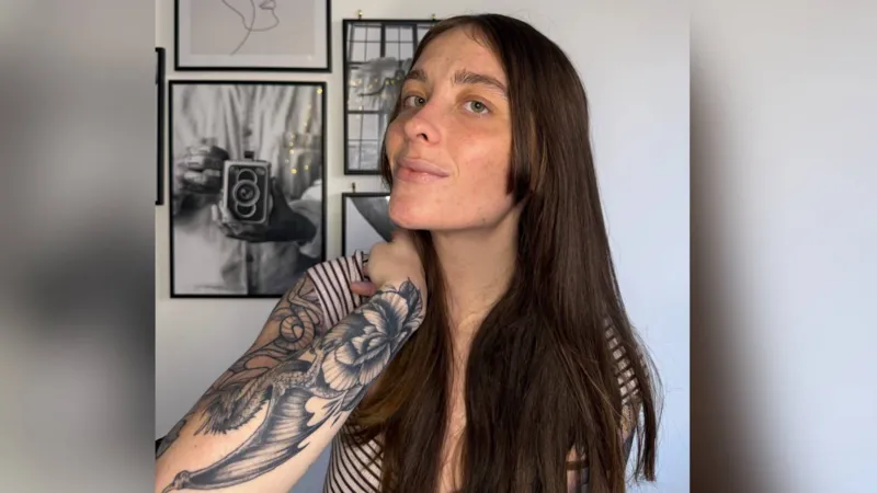 Lili Hope Photograph of Lili Hope, 22, showing her dragon tattoo on her forearm. She has brown long hair, blue eyes and smiles at the camera.