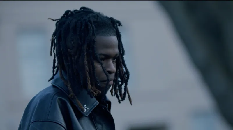 Lindsay Entertainment Jordan Adetunji. Ia memiliki rambut gelap panjang sebahu, mengenakan jaket kulit hitam. Ia menoleh ke samping.