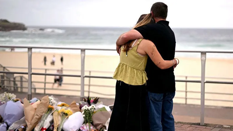 A couple standing on a promenade with a floral tribute, the beach and ocean in the distance